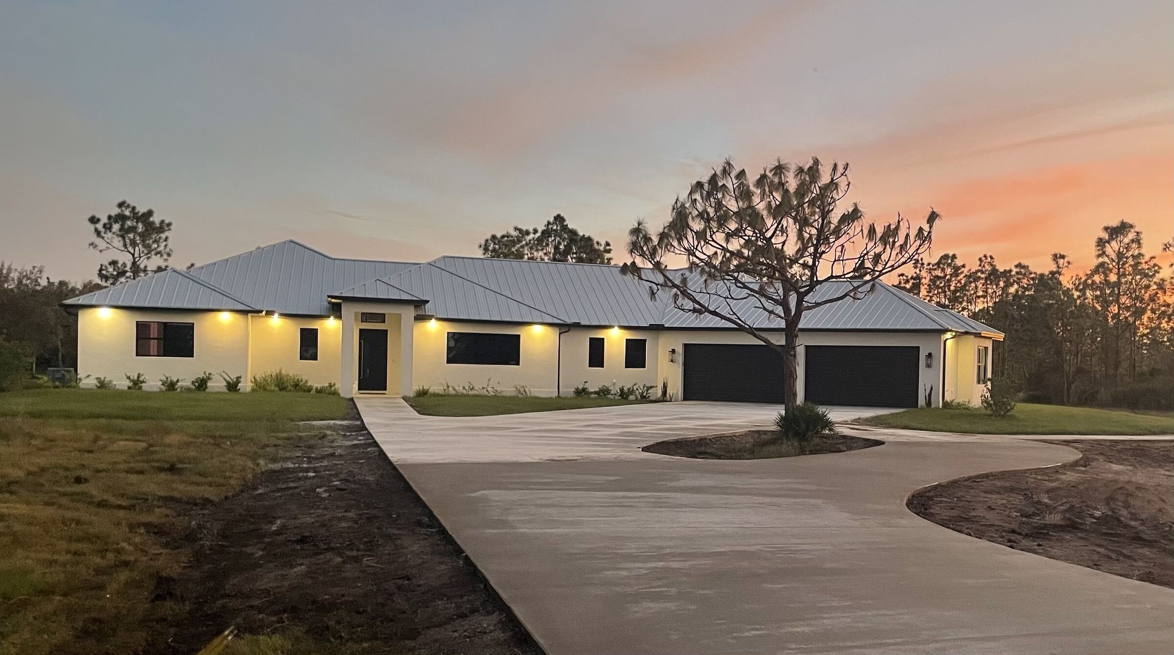 Custom home built by Beach Star Construction, photographed at dusk with a standing-seam metal roof and lit entry